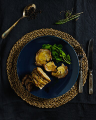 Roast beef with black peeper and rosemary, on a dark tablecloth and silverware

