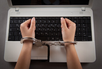 Hands and handcuffs on laptop keyboard. Cyber Crime.