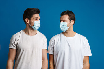 Pleased brunette two guys in face masks posing and looking at each other