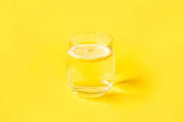 Glass of water with lemon on a yellow background. Summer refreshing drink.