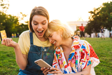 Image of excited two women holding credit card and using cellphone