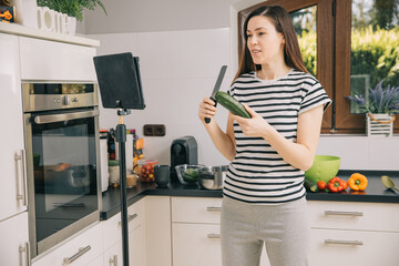 Young woman shows online how to prepare healthy and tasty food at home. Blogger takes a video in her kitchen. Online healthy eating courses. Video blog from home during the pandemic. 