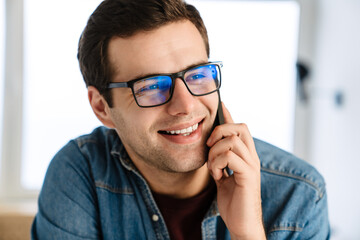 Happy handsome man in eyeglasses smiling and talking on mobile phone