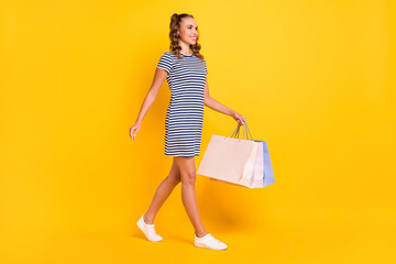 Full length body size view of pretty cheerful girl walking carrying new things bags outlet isolated on bright yellow color background