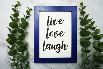 Live Love Laught written on blue frame with green leave flat lay on marble background