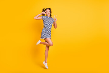 Photo of pretty sweet young woman wear striped clothes jumping showing v-signs empty space isolated yellow color background