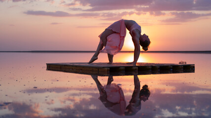 gymnastics, flexibility, freedom.  The girl performs a back bend against the background of a golden sunset on a pink lake