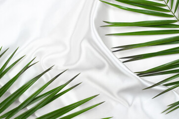 Beautiful background of white silk fabric with green palm branches. Wavy fabric texture with place...