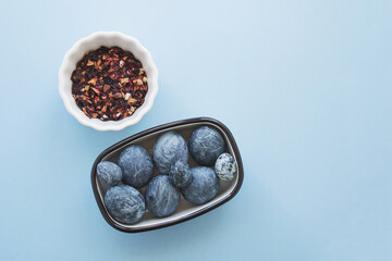 painting eggs for the Easter holiday with hibiscus carcade tea, blue background, a bowl of dry tea, blue marble space eggs with an abstract pattern, preparing for the holiday, place for text 