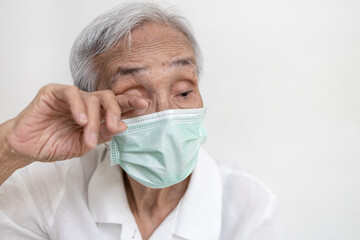 Asian senior woman in medical protective mask rubbing her eyes,Do not touch eyes with her dirty hand,avoid touching to protect form COVID-19,risk of Coronavirus infection,Don't touch face,health care