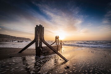 Sunrise at The Warren, Folkestone. A winter sunrise lights the sky behind the old sea groynes on The Warren at low tide. These groynes are only visible when the tide is out. They show evidence of the 