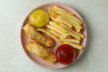 Plate with fried fish and chips, and sauces on white textured background