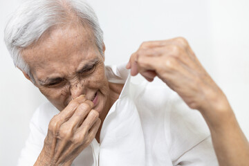 Fototapeta premium Old elderly people is sniffing shirt smell moldy,closing nose with the disgusting,intolerable smell,dirty laundry,unclean washing,problem of clothes smell musty,unpleasant effects in the rainy season