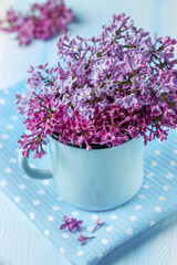 Bouquet of lilacs in mug on blue wooden background