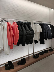 Rack with clothes on hangers and shoes in the store against the background of a small wall.