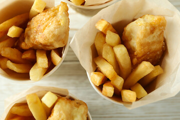 Paper cups with fried fish and chips on wooden background