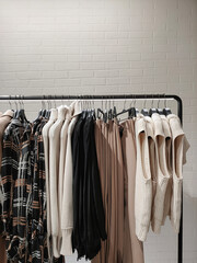 Rack with clothes on hangers in the store against the backdrop of a wall.