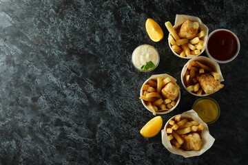 Paper cups with fried fish and chips, and sauces on black smokey background