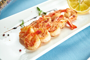 Appetizing grilled Mediterranean shrimp with lemon in a white plate on a blue tablecloth