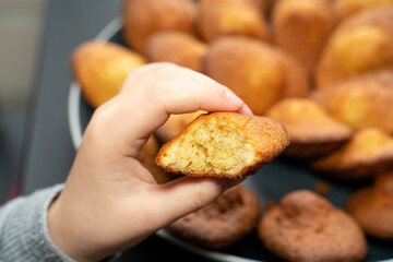 enfant tenant une madeleine petite pâtisserie fait maison devant une assiette remplie de madeleines fraîches