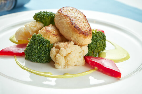 Diet turkey cutlets garnished with steamed vegetables in a white plate on a blue tablecloth.