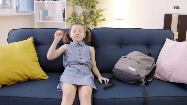 Tired schoolgirl putting backpack on the sofa, relaxing at home after lessons