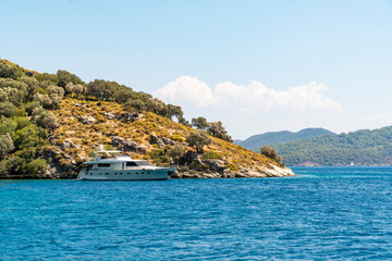 Summer concept: Luxury yacht boat anchored stern in a bay with blue turquoise waters. View from land with green trees and sea in background with copy space