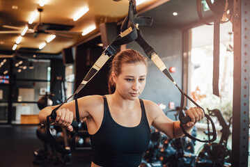 Fototapeta na wymiar Portrait of a caucasian sportswoman in black shirt doing physical exercise with a training apparatus in gym in daytime.