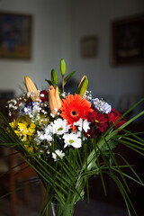 Bouquet of flowers in a glass vase in a living room as a decoration with chairs, tables and pictures in the background. colorful flowers