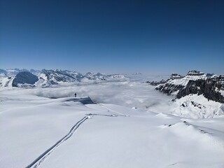 Fototapeta na wymiar Ski tour in the Swiss mountains. View of the snowy mountains above the clouds. Fantastic views and a powder run. Glarus. Skimo