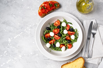 Typical dishes of the Mediterranean diet : mozzarella balls, black olives, olive oil, salad with tomatoes and arugula, bruschetta. Healthy Food Italian cuisine. 