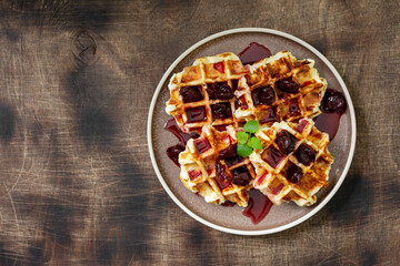 Belgian or Brussels waffles with cherry jam. Homemade wafer in a large plate on a brown wooden table