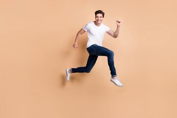 Fototapeta na wymiar Full size profile photo of hooray brunet man jump run wear t-shirt jeans sneakers isolated on beige background