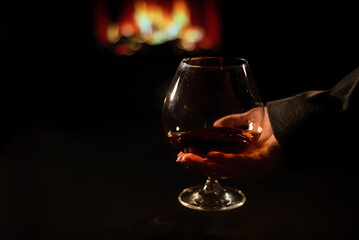 Close-up of a female hand with a glass of brandy on the background of the fireplace