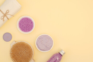 Cosmetic set for spa treatments at home. Bath salt, home body scrub, pearl sea salt with lavender, white towel, candle aroma, anti-cellulite massage brush on yellow background with copy space, top