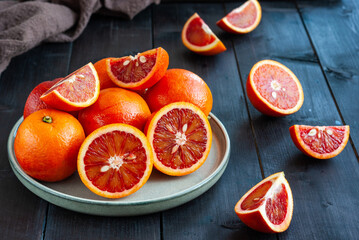 Sliced and whole ripe sicilian red oranges on dark wooden background