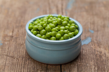 Green peas in blue bowl on rustic wooden background