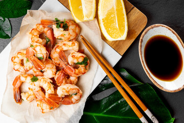  Fried shrimps with lemon and soy sauce on a white cutting board and green monstera leave close up, top view
