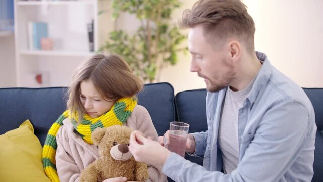 Young father offering sick daughter to drink pill, treatment of virus, medicine