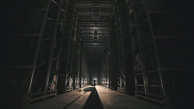 Turning on lighting in a factory warehouse. Morning in the factory, a man walks through the warehouse light turns on