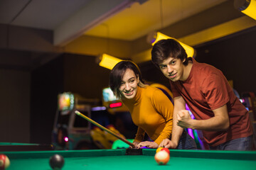 Young couple spending time in billiard room. Man supporting his girlfriend.