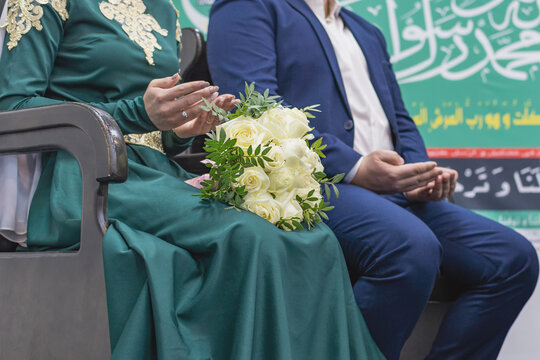 Nikah is a Muslim wedding ceremony. The bride and groom sit next to each other, hands folded in prayer. A bouquet of roses lies on the girl's lap. 