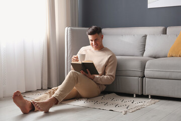 Man with cup of hot drink reading book at home. Floor heating concept