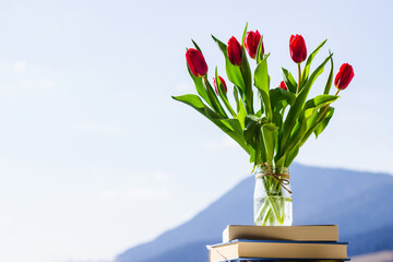 bunch of tulips in a glass vase against blue sky, colorful spring flowers on blurred background with free copy space, springtime concept
