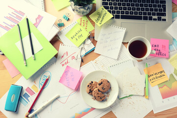 Messy table with laptop, cookies and tea, flat lay. Concept of being overwhelmed by work