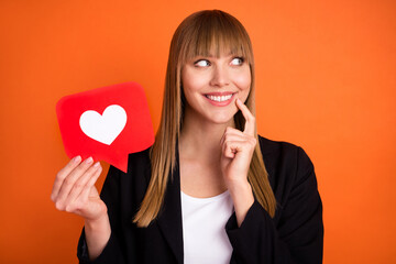 Portrait of beautiful trendy dreamy cheerful girl holding paper red card web like thinking isolated over bright orange color background