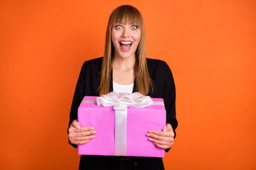 Portrait of attractive amazed cheerful girl holding in hands giftbox having fun isolated over bright orange color background