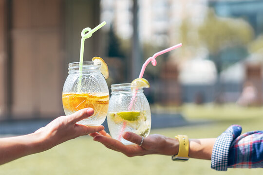 Human hands in the summer sunny city day drinking a cocktail from glass jars.