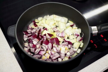 Red and white onions are fried in a hot frying pan. Cooking the dish