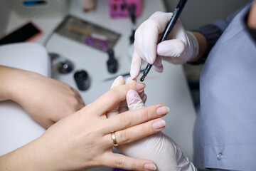 Manicurist applies gel polish to the client's nails. The manicure master works with a brush and nail polish